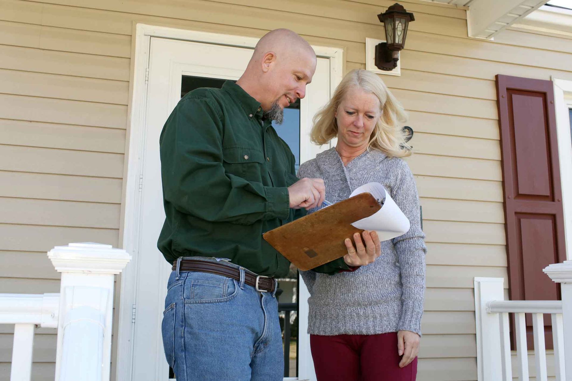 A man and a woman are standing in front of a house looking at a clipboard.