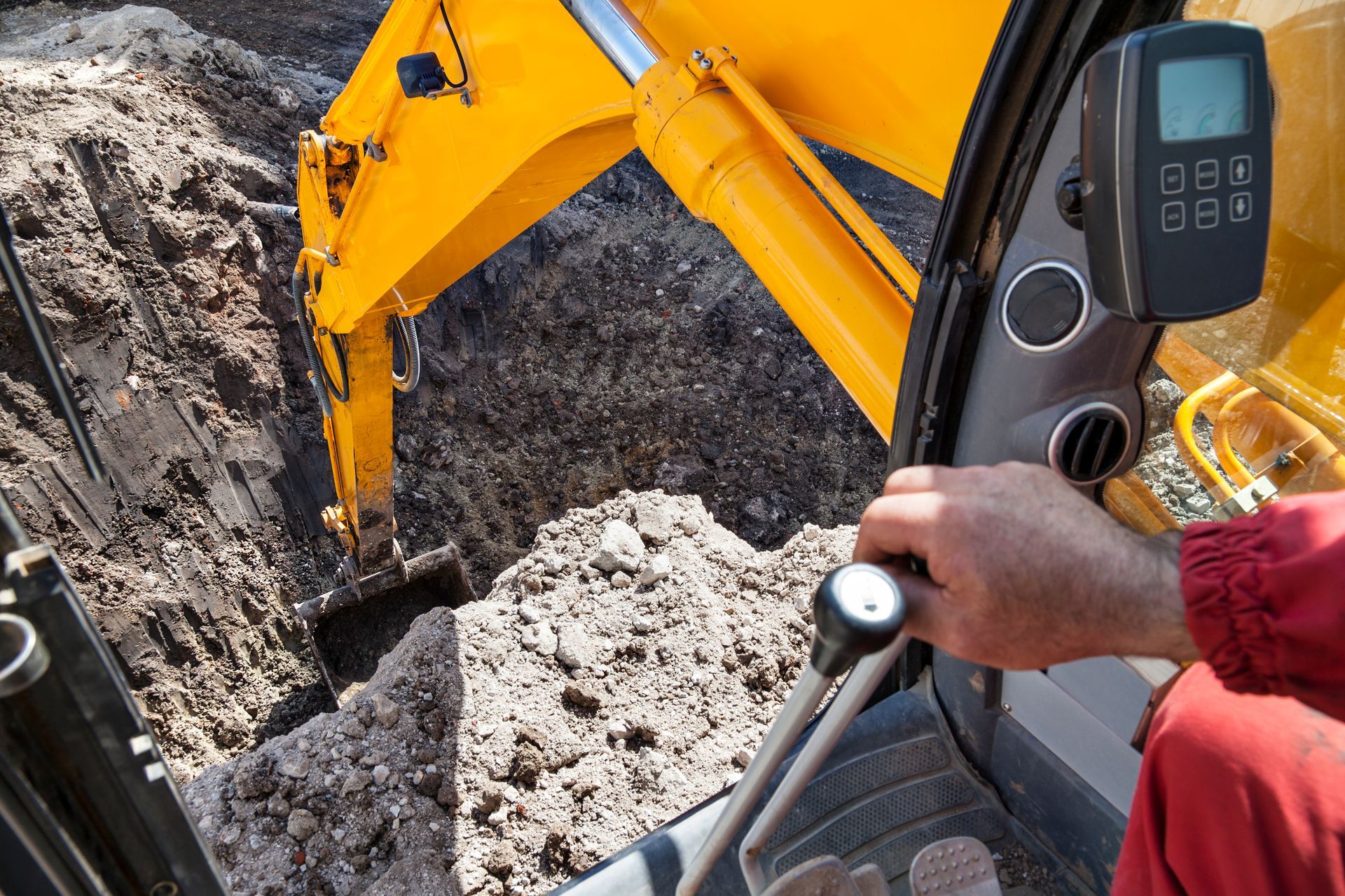 A person operating a yellow excavator, digging a trench, close-up of the interior and controls.