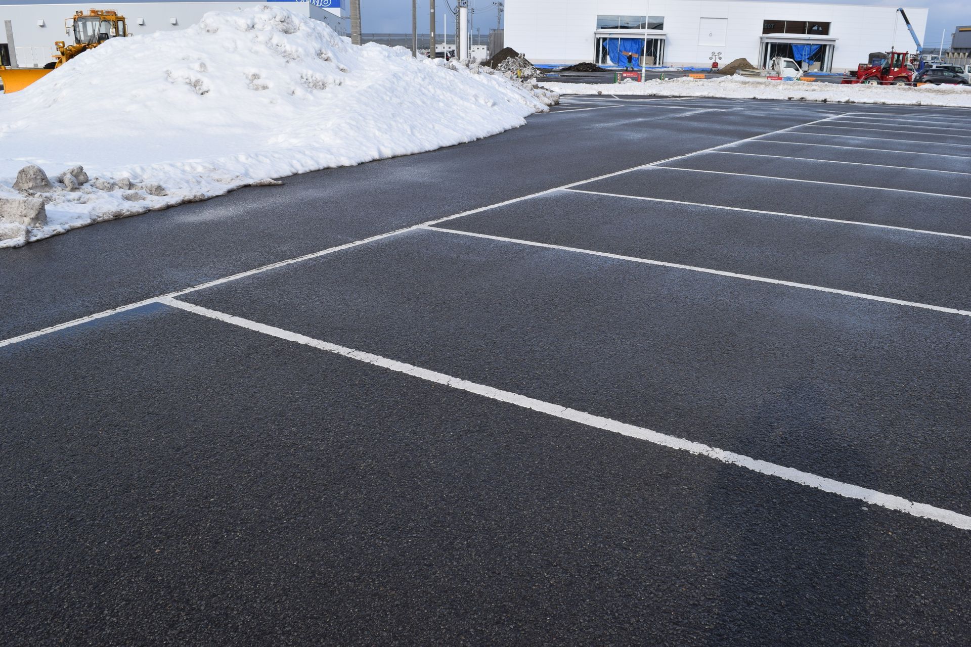 Empty asphalt parking lot with white painted lines and a large pile of snow.