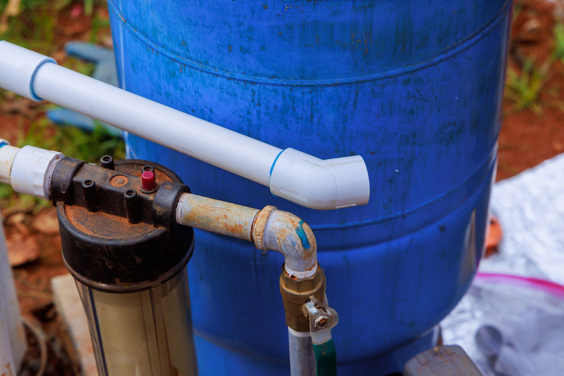 Blue water tank with white and rusty pipes and a filter in an outdoor setting.