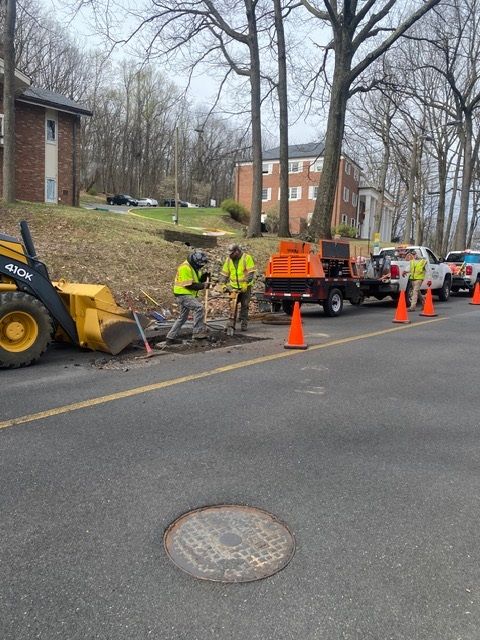 Road workers spread asphalt with tools next to a steamroller.