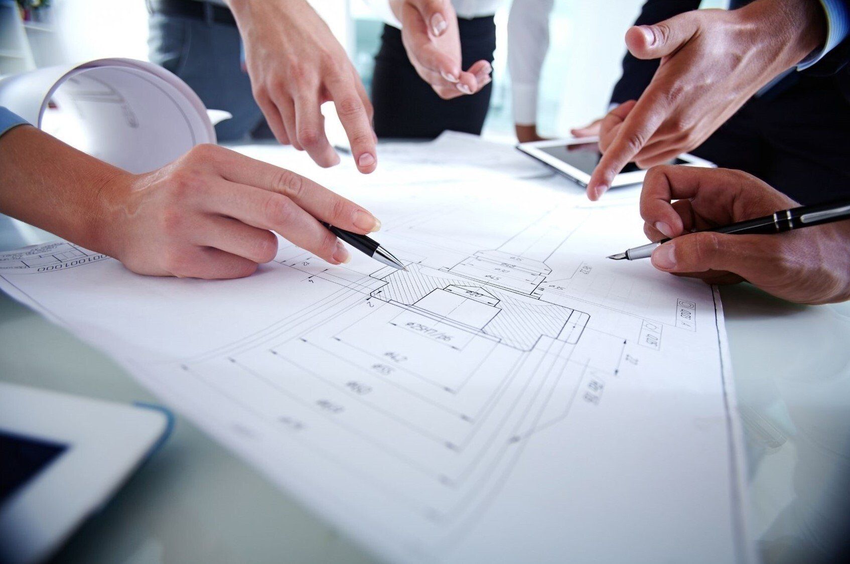 people meeting around drawing with pens pointing to areas on the drawing