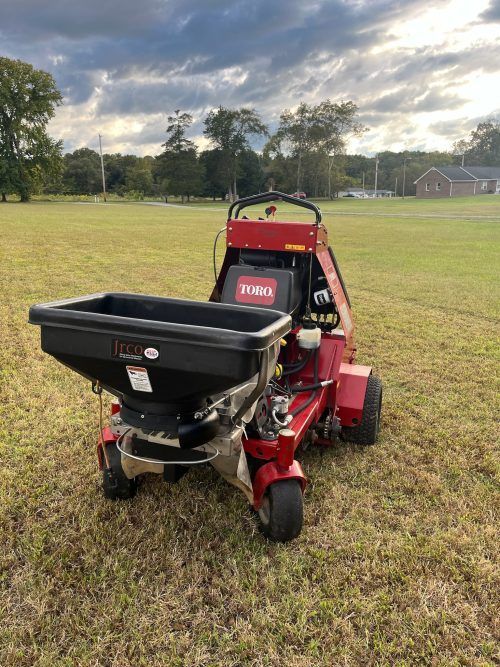 A lawn mower with a spreader attached to it is sitting on top of a lush green field.