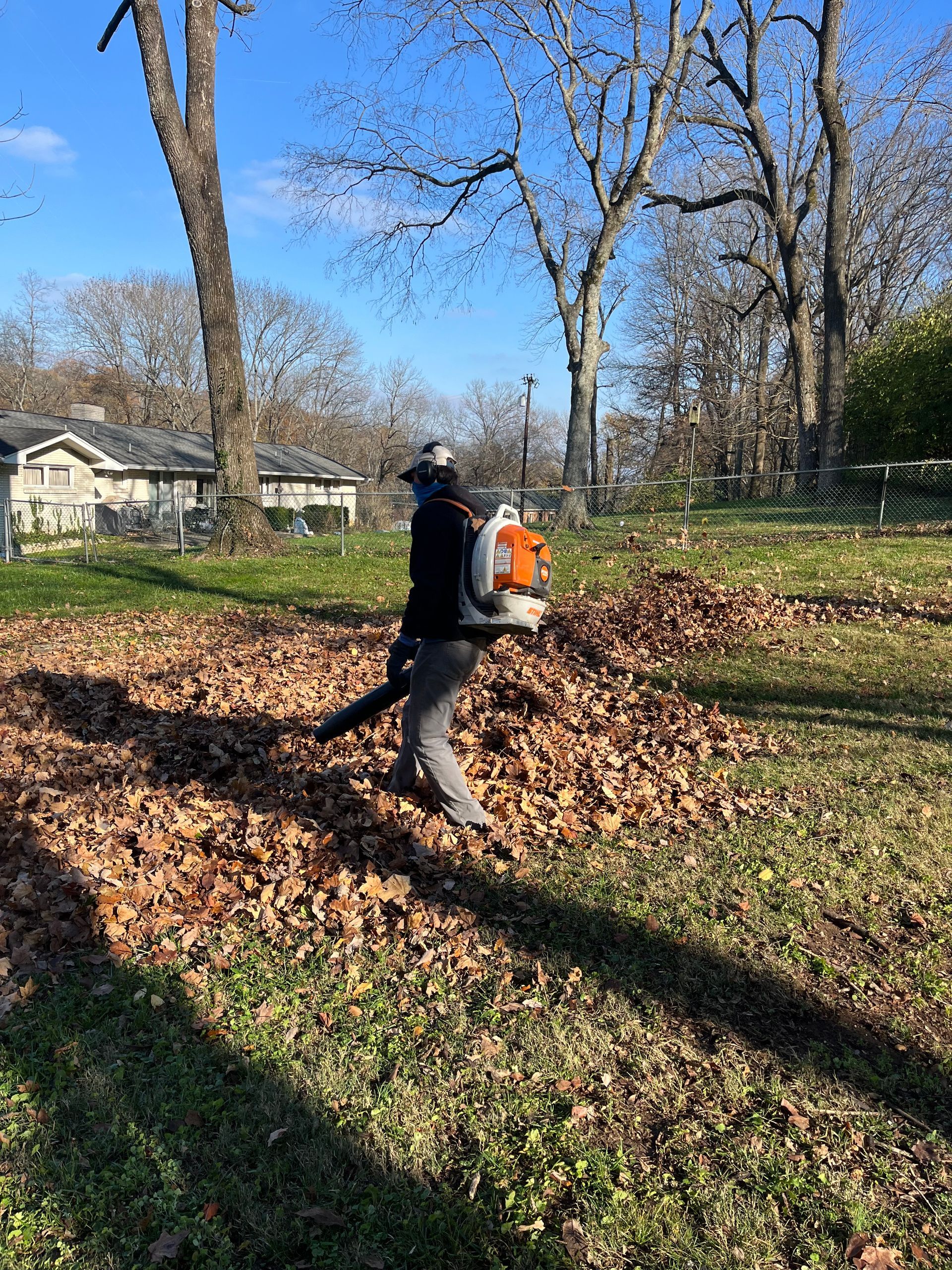 A man is blowing leaves in a park with a backpack blower.