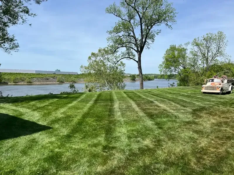 A lawn mower is cutting a lush green lawn next to a river.