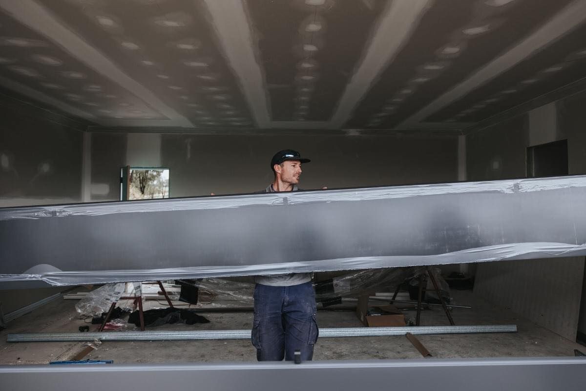Construction worker inside a room holding a large metal beam, working on the ceiling.