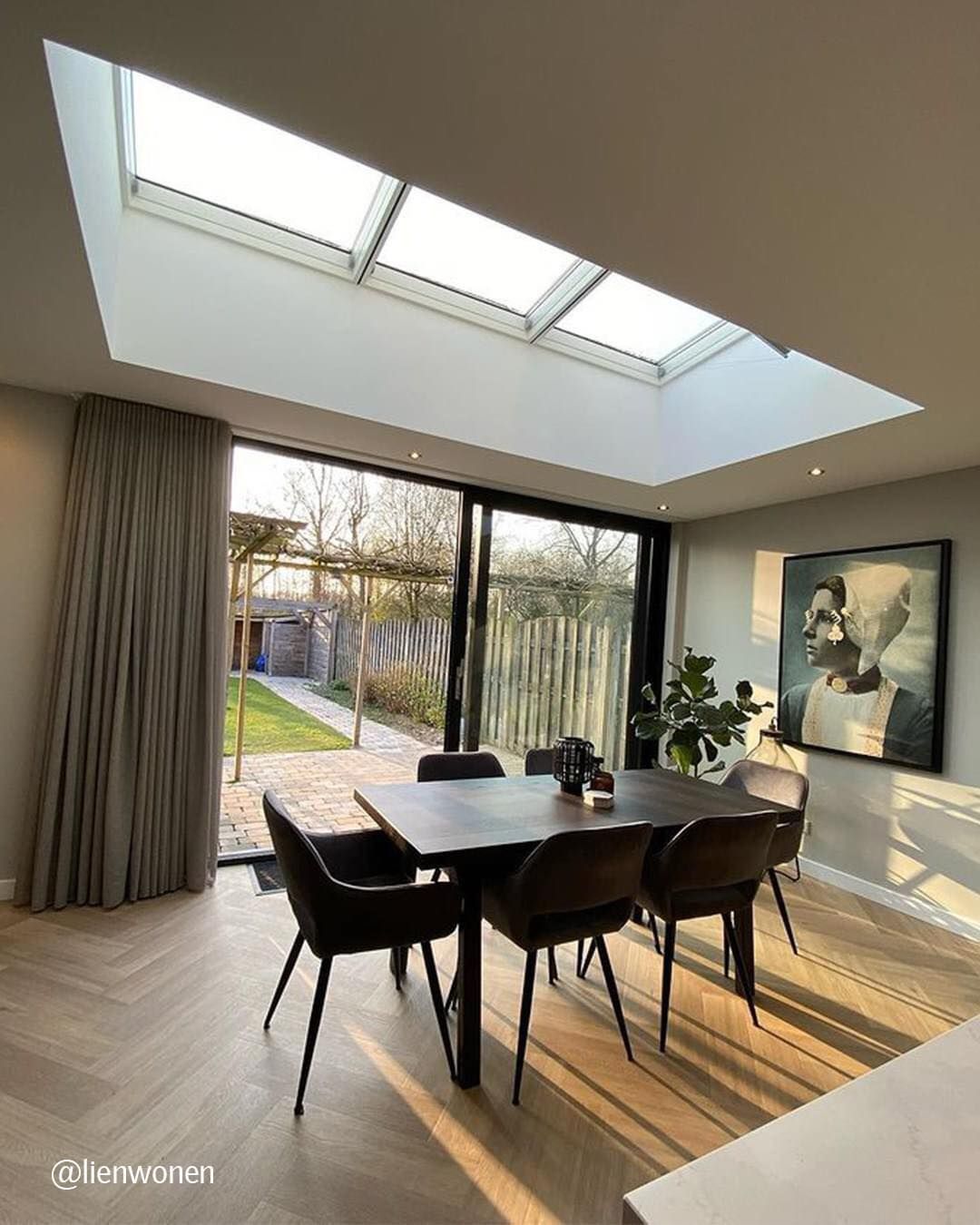 Dining room with skylights, large windows, dark table, chairs, and garden view.
