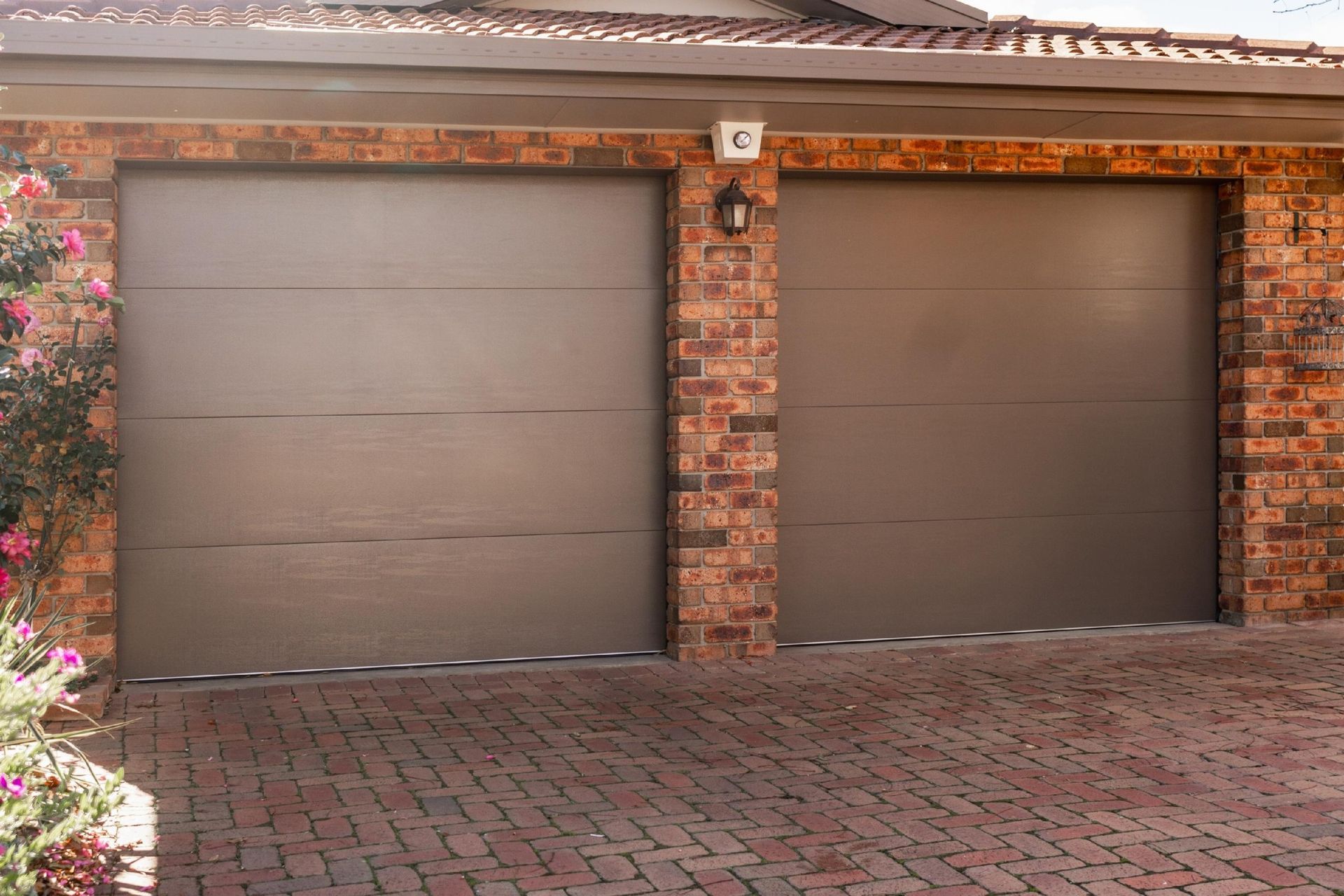 Two gray garage doors with brick columns in a residential setting.