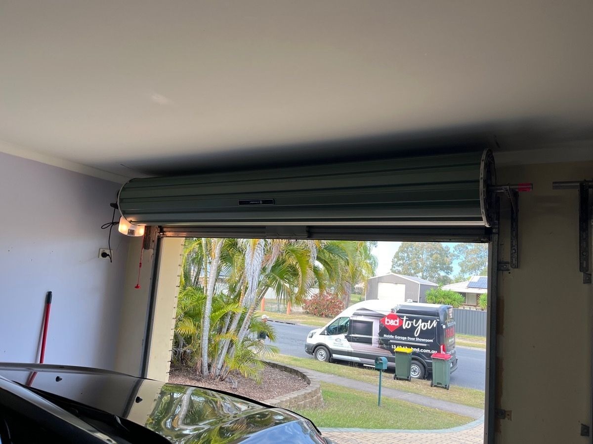 Garage door partially open, revealing a street scene and vehicle. The door is green.