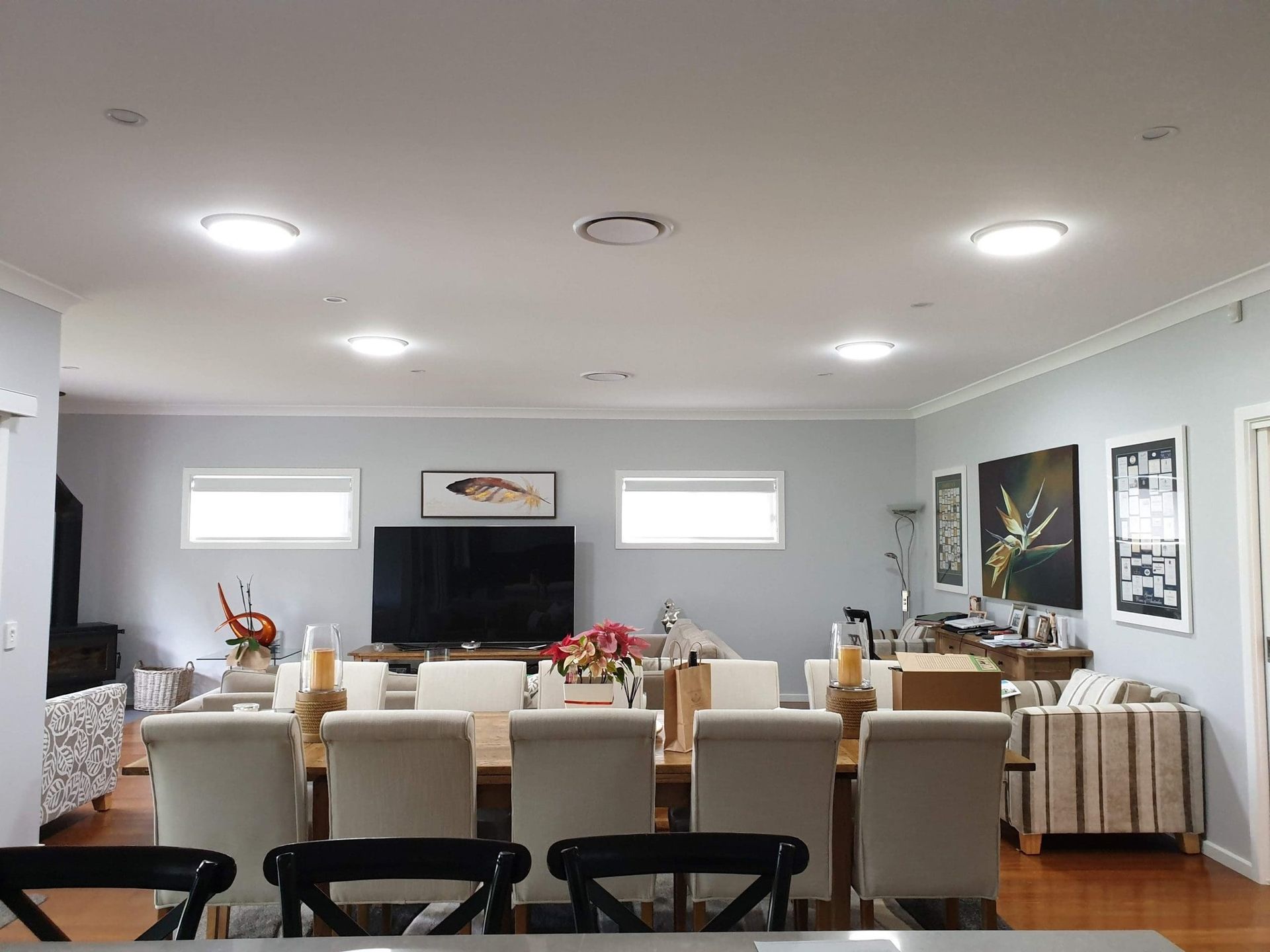 Spacious dining room with long wooden table, white chairs, artwork, and recessed lighting.