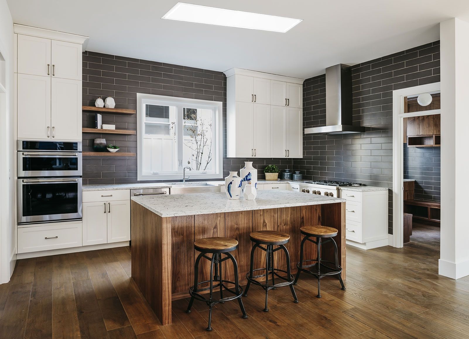 Kitchen with white cabinets, wood island with stools, and dark tiled backsplash.