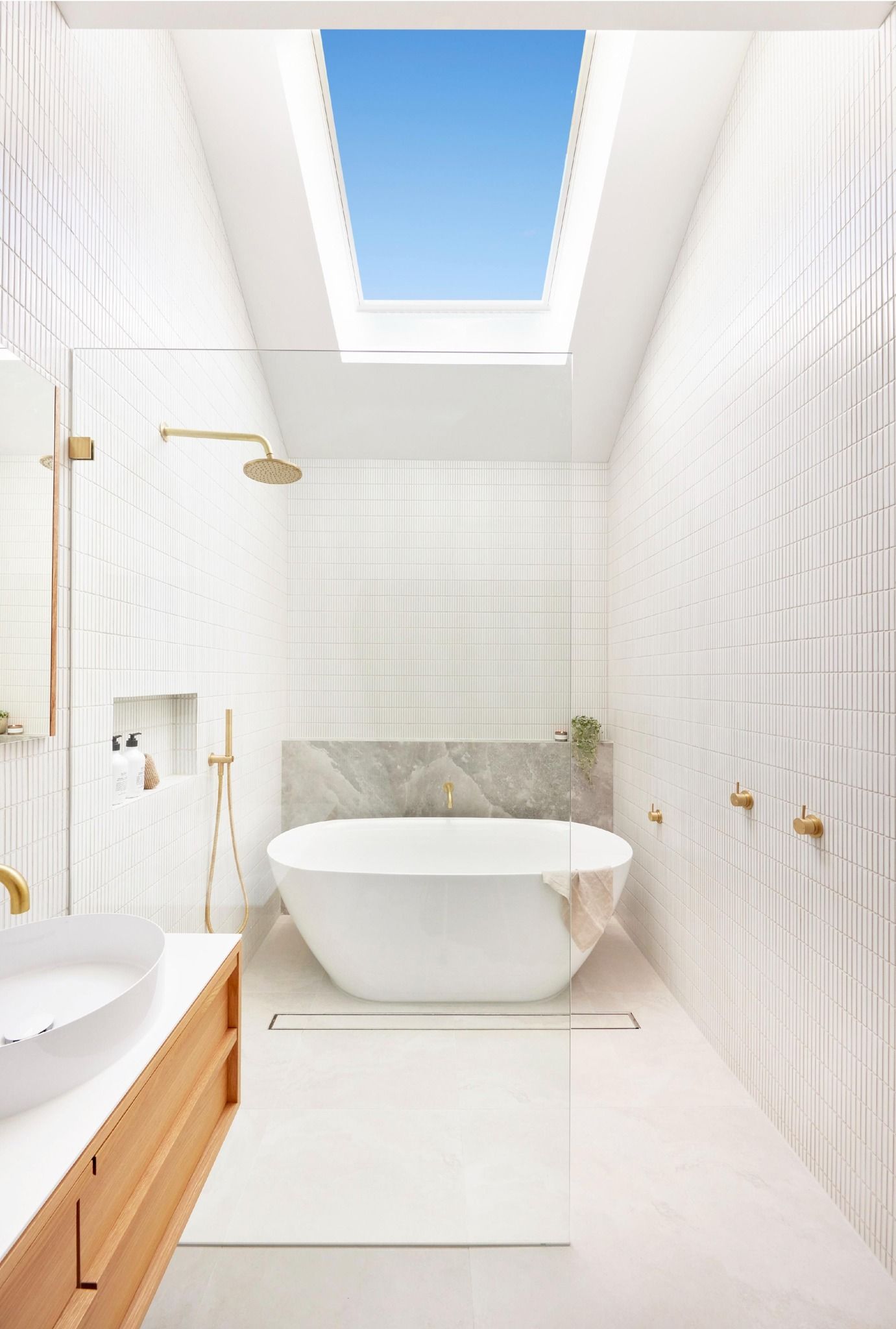 Bright white bathroom with a skylight, a soaking tub, and gold fixtures.