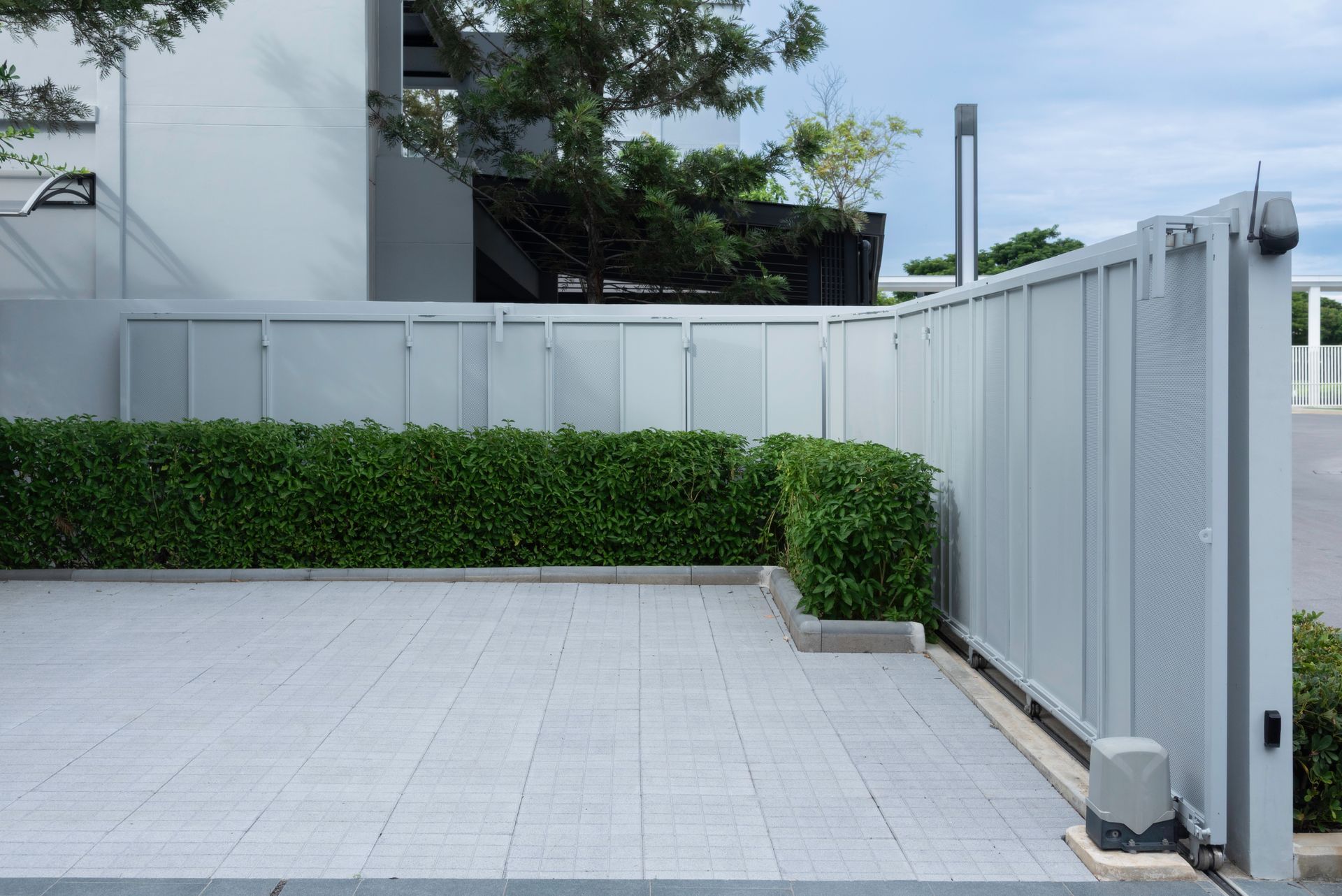 A gray tiled patio area enclosed by a matching fence and green hedges.