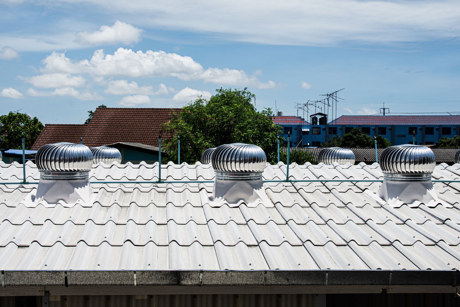 Metal roof with several rotating vents, blue sky with clouds in background.