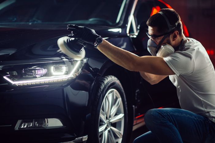 Mechanic inspecting a black car’s headlight in a dim garage with a handheld light