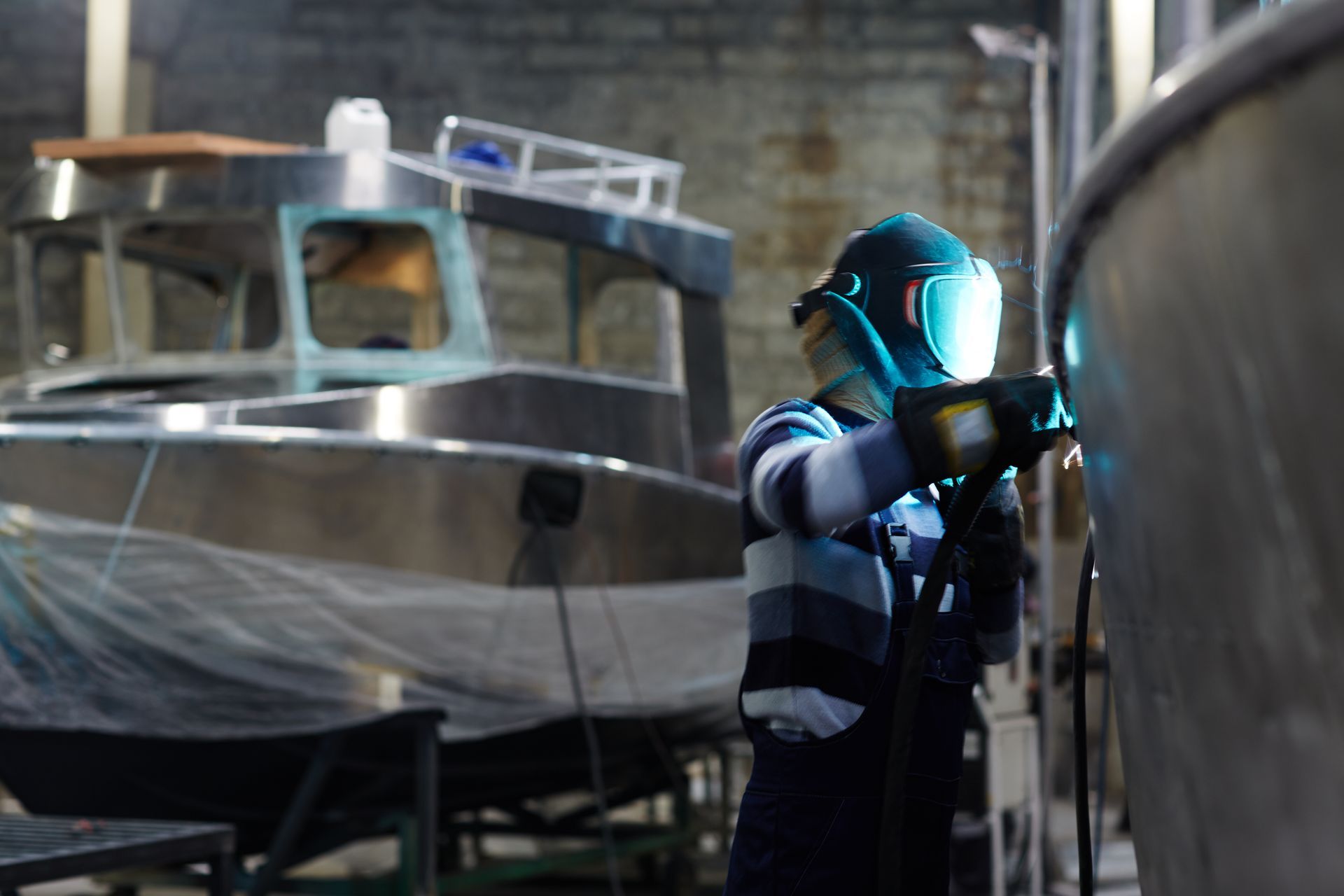 Person in blue workwear painting a boat in a shipyard