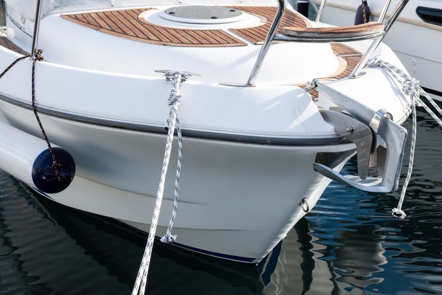 White sailboat bow docked on dark water, with anchor line and ropes tied off at the front.