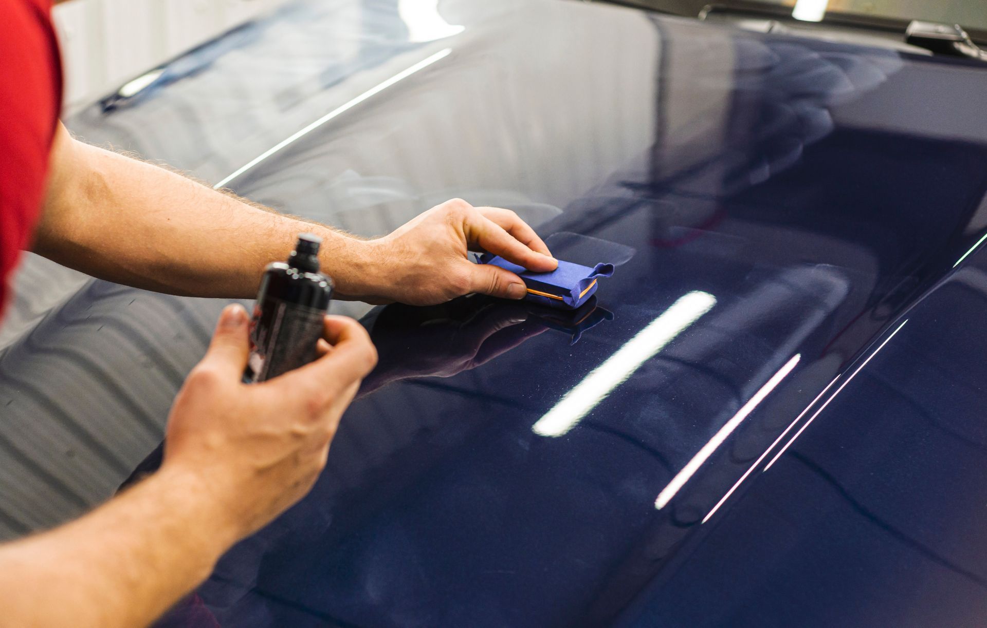 Hands polishing a dark blue car hood with a cloth and spray bottle