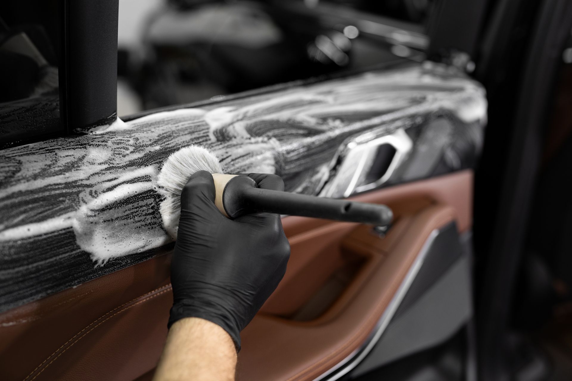 Gloved hand scrubbing a car door with a brush, cleaning white residue from dark paint