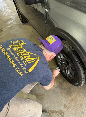 Person cleaning a black car’s wheel with a cloth in a garage or driveway.