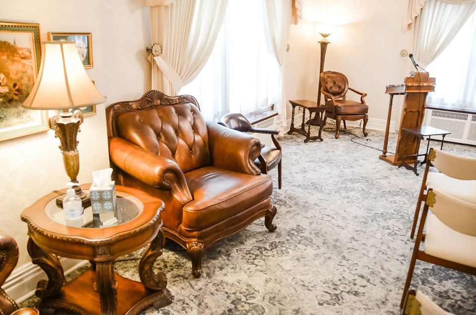 A living room with a chair , table , lamp and podium.