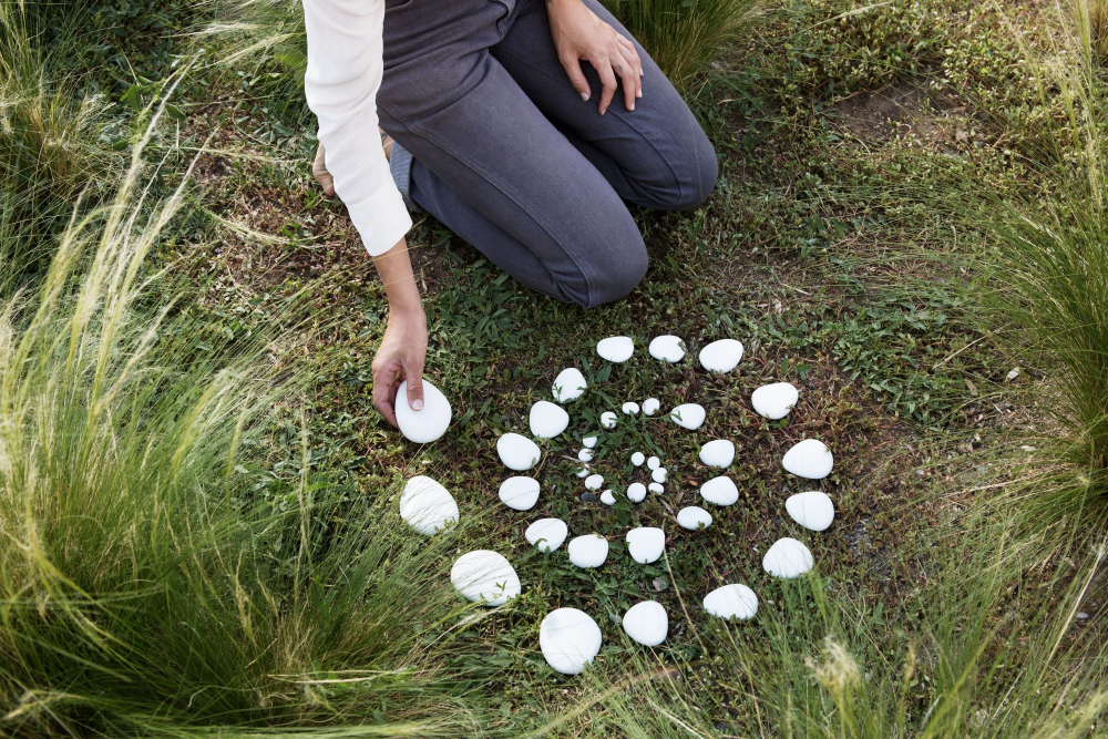 A woman is kneeling in the grass making a circle with white rocks.