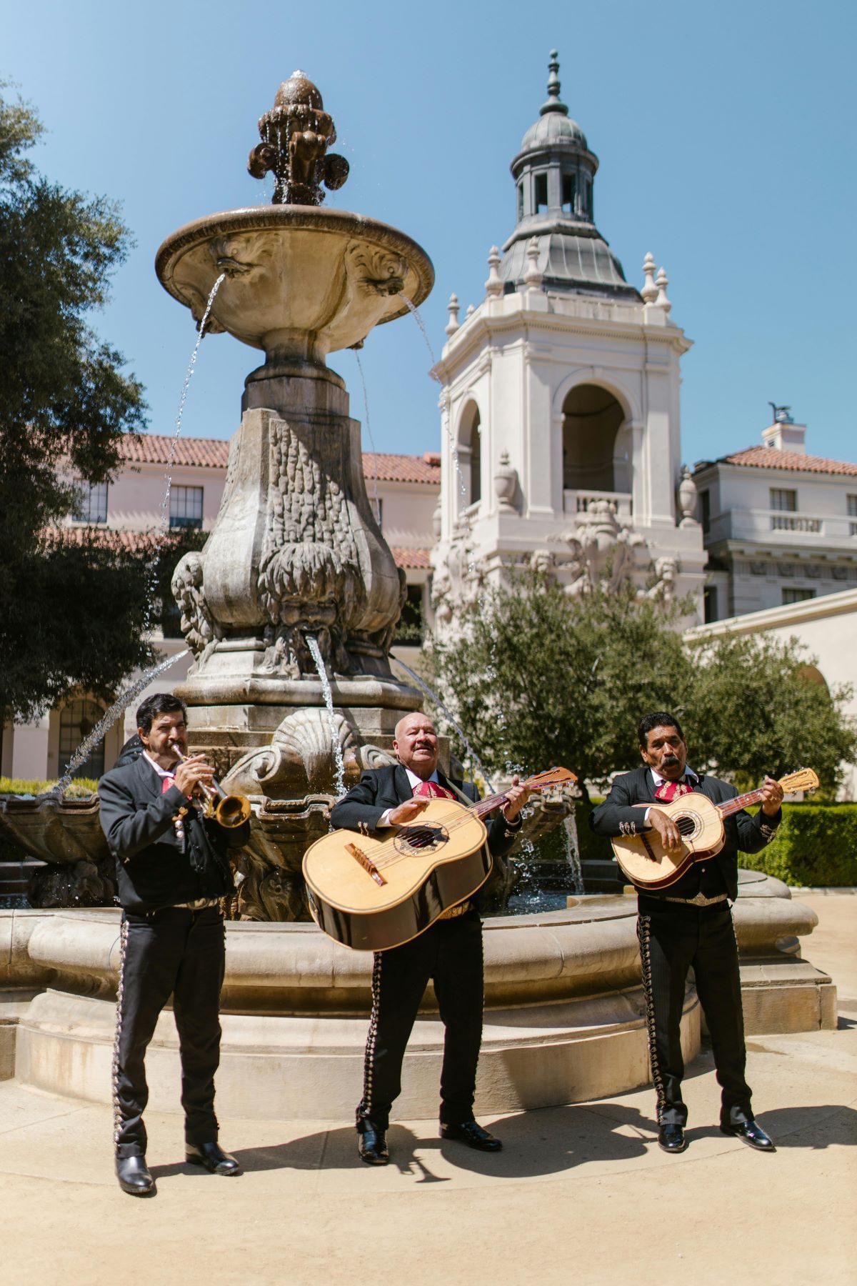 Three men are playing guitars in front of a fountain.