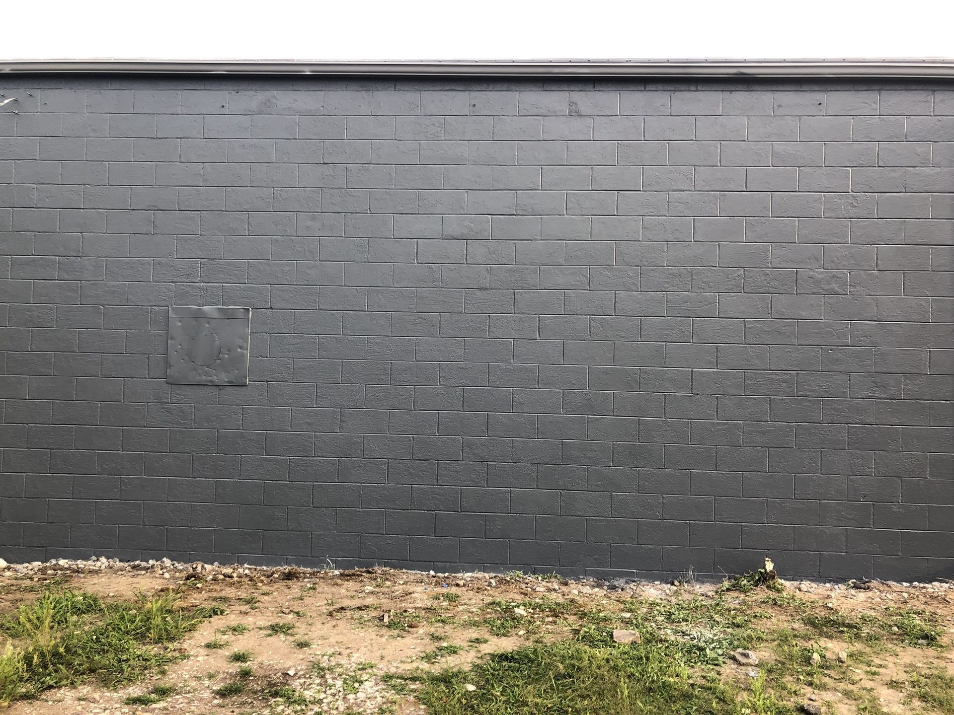 A black brick wall is surrounded by grass and dirt.
