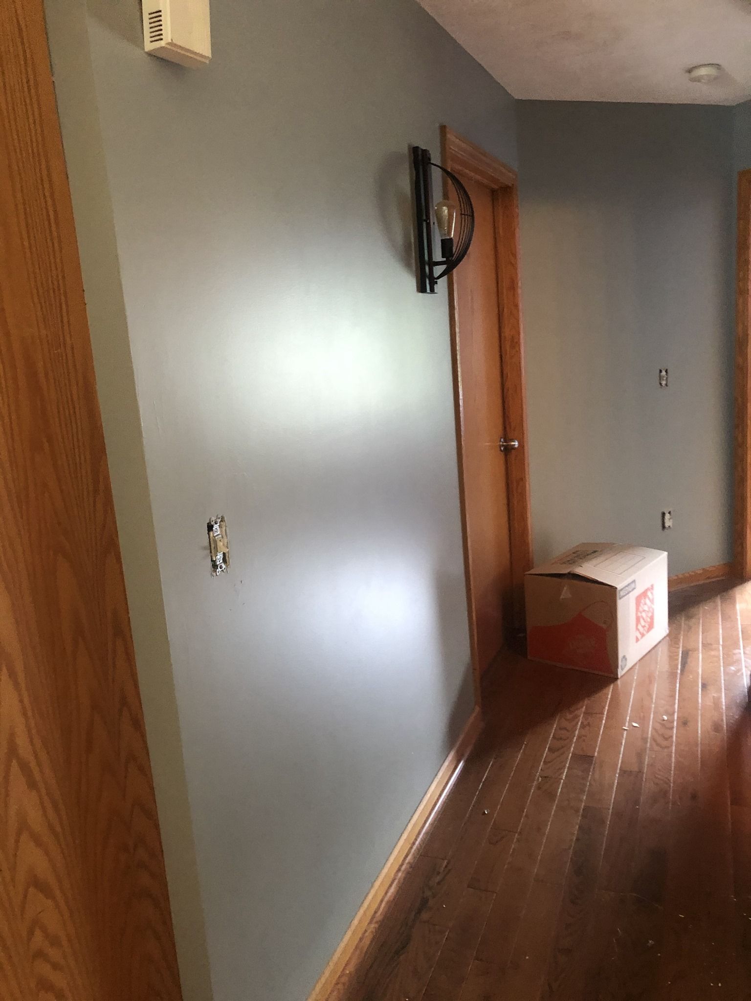 A hallway with a box on the floor and a light on the wall.