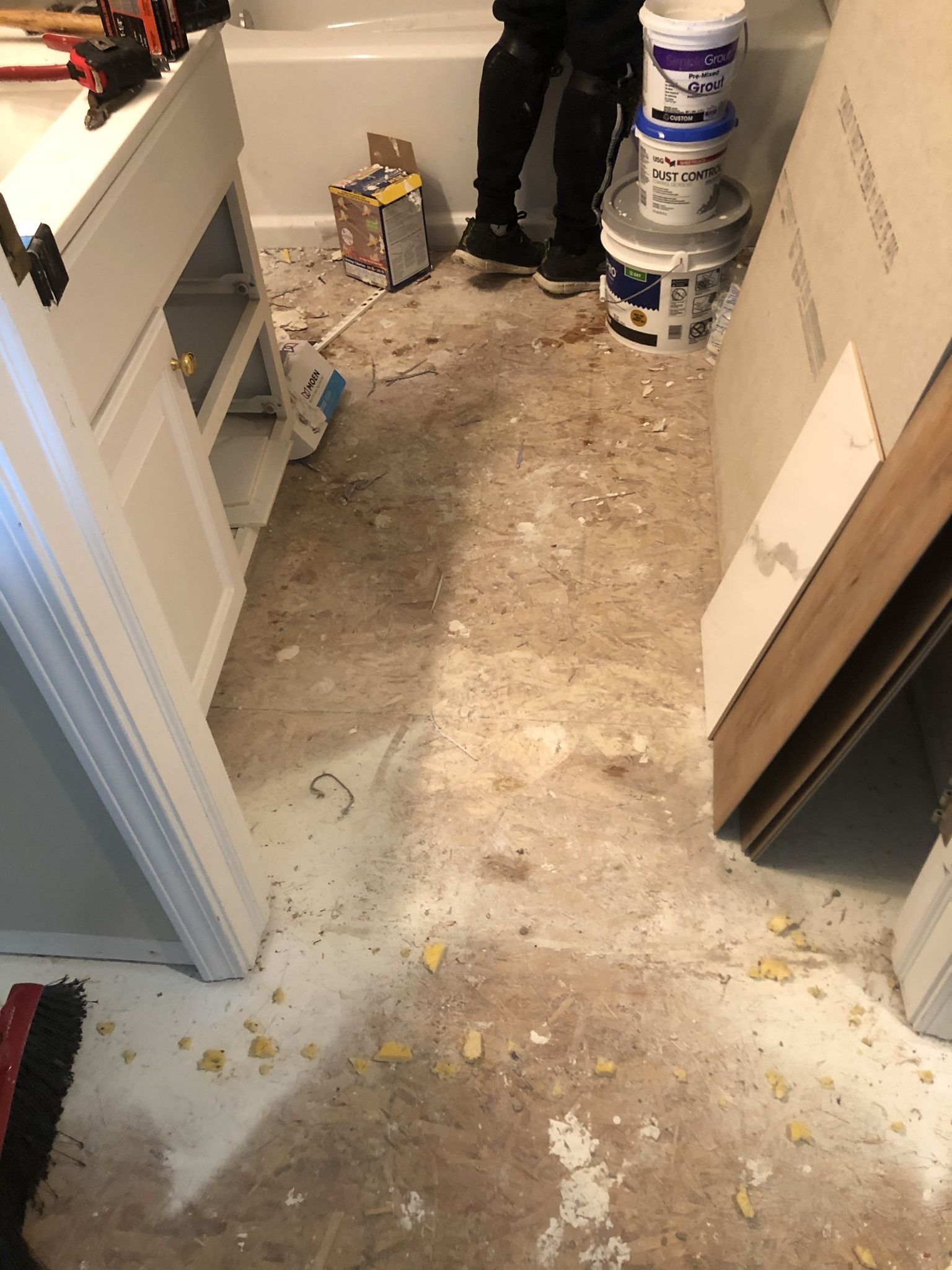 A person is standing in a bathroom with buckets of paint on the floor.