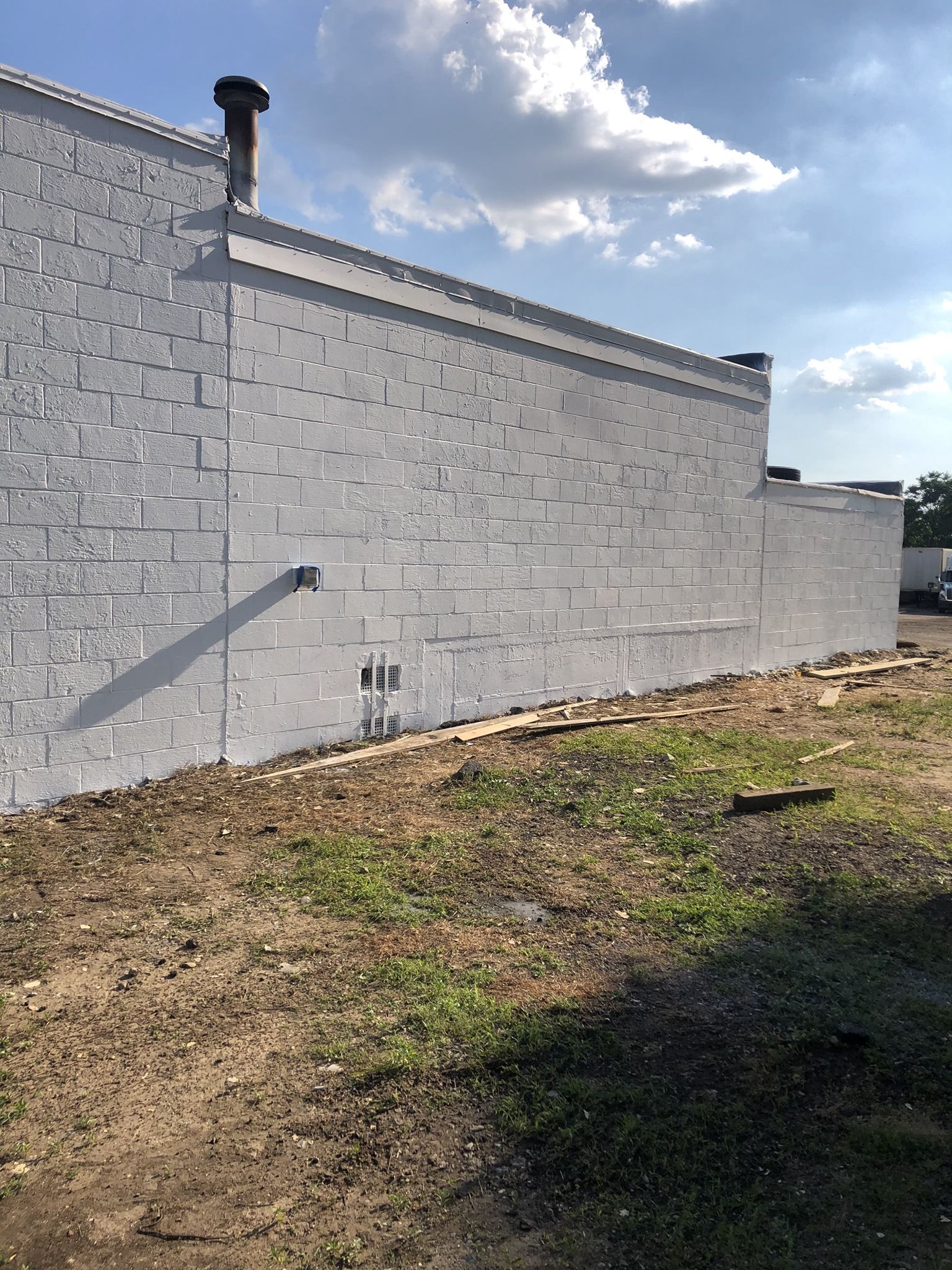 A large white brick wall is surrounded by grass and dirt.