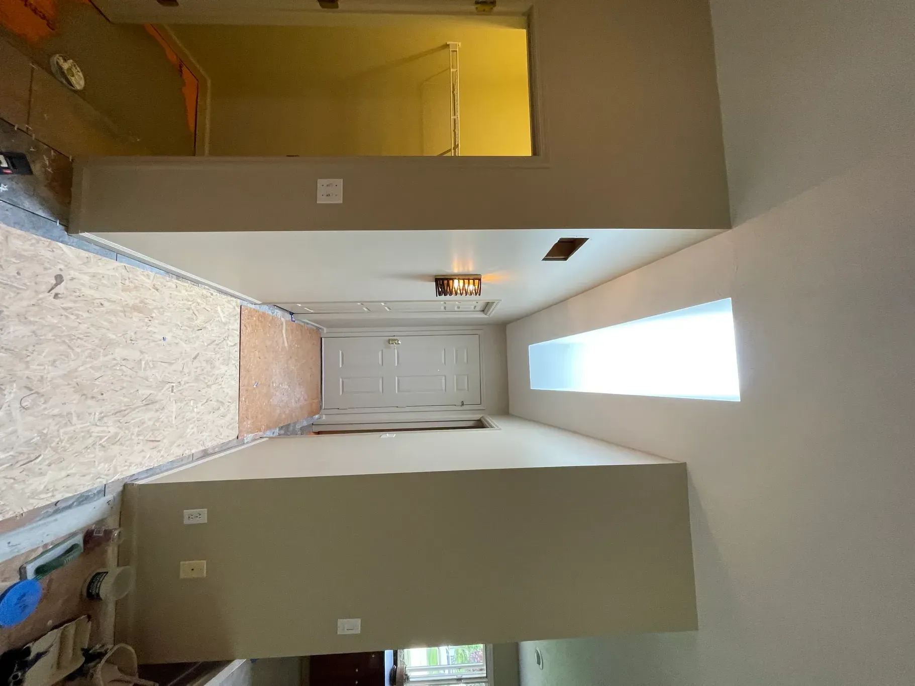 A long hallway in a house with a window and a door.