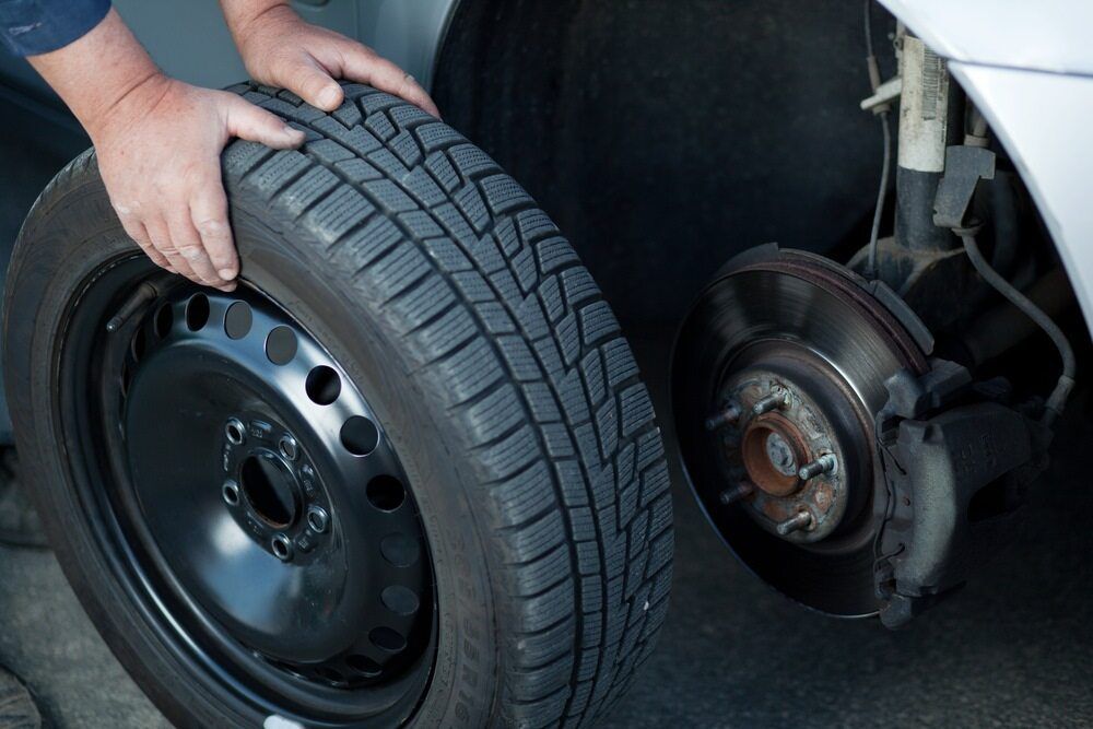Person Changing A Car Tire; Holding A Black Tire, Car Wheel With Brake Visible