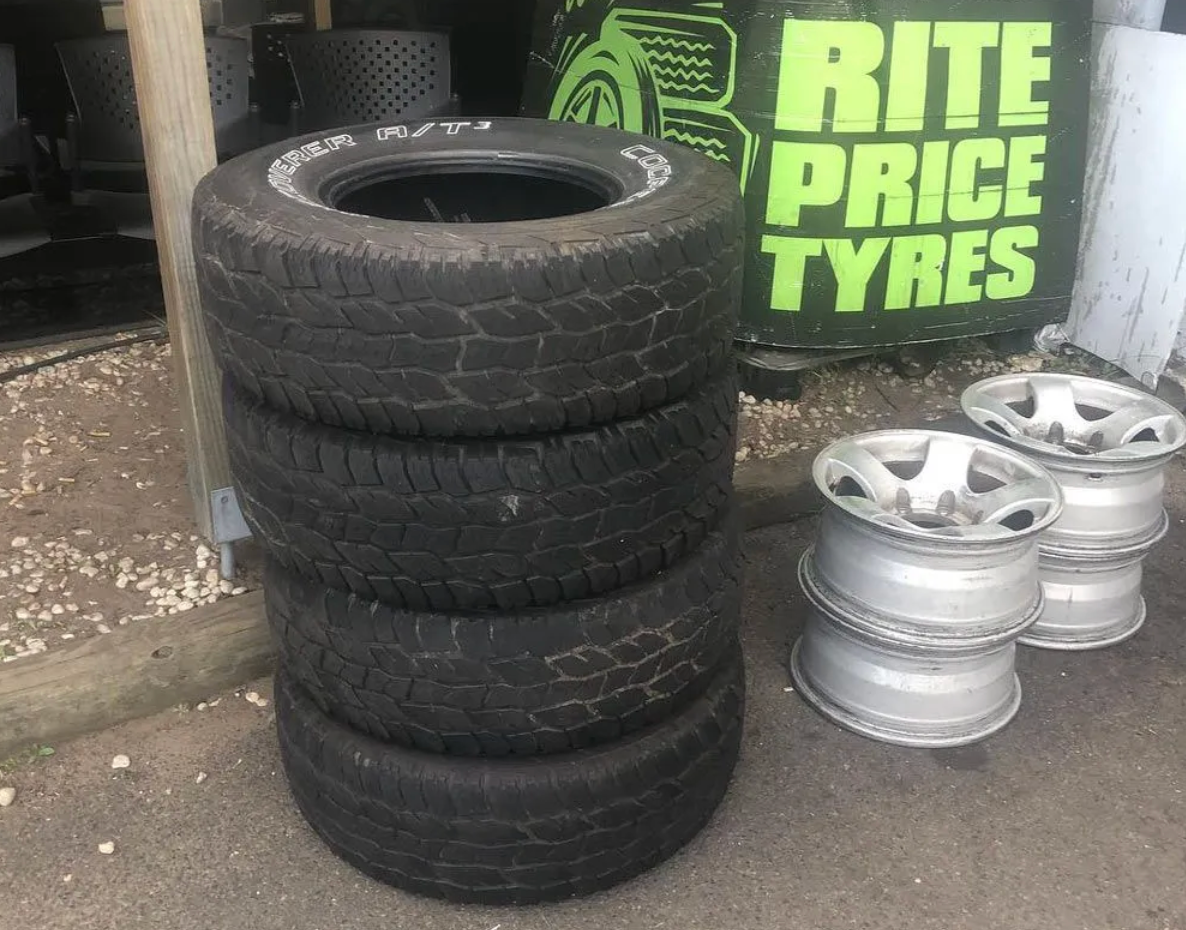 A stack of black, rubber tyres next to a stack of car rims and a 'Rite Price tyres' sign.