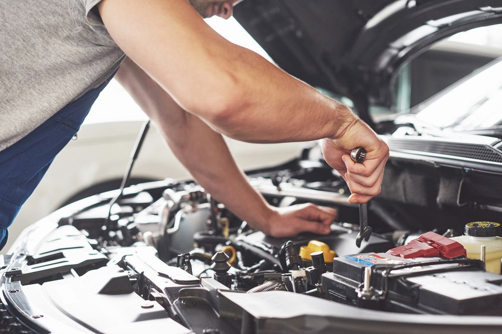 A Man is Working on the Engine of a Car With the Hood Open — Rite Price Tyres In Tuggerah, NSW