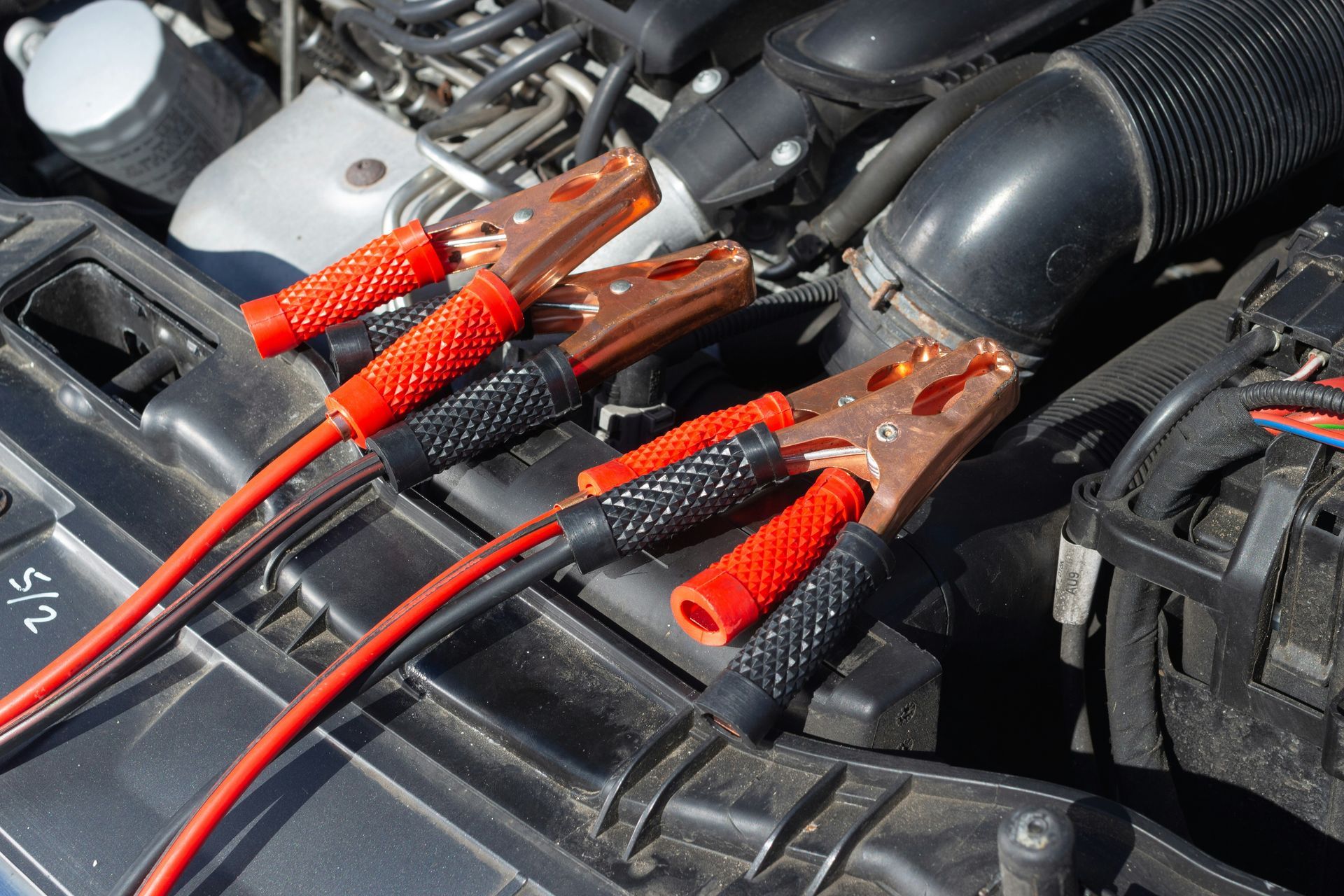 Startkabels zijn aangesloten op de accupolen van de auto in de motorruimte. De rode en zwarte kabels zijn zichtbaar.
