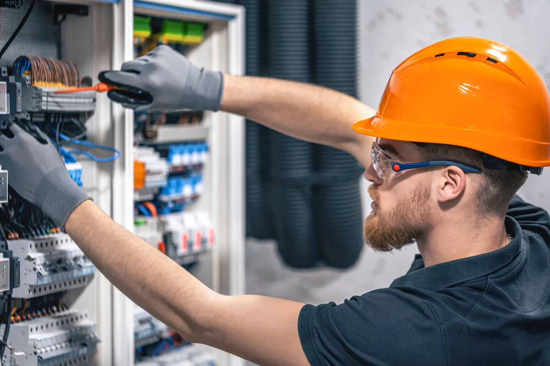 A man wearing a hard hat and safety glasses is working on an electrical box.
