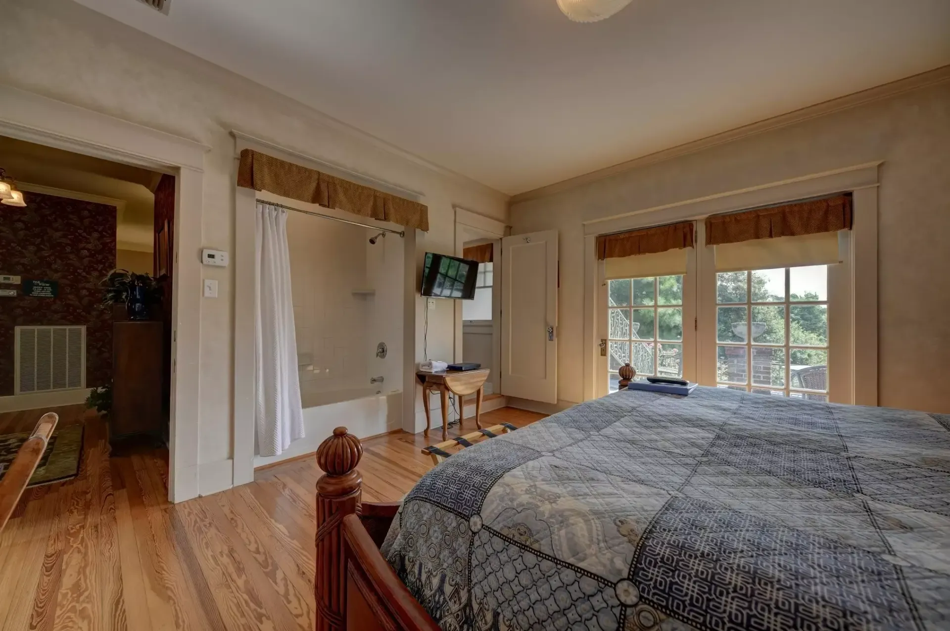 Bedroom with bed, bathroom, and French doors leading to a balcony. Blue and white quilt on the bed.