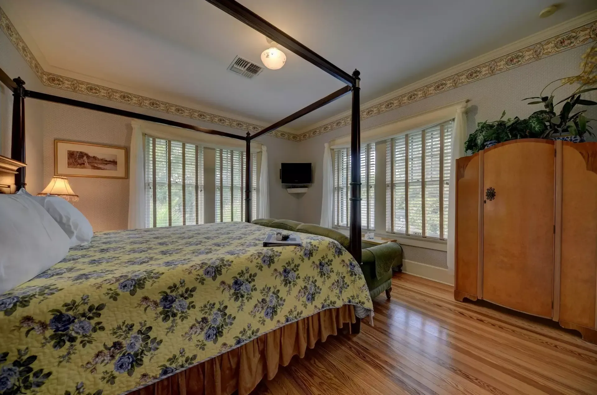 Bedroom with four-poster bed, patterned quilt, wooden wardrobe, and shuttered windows.