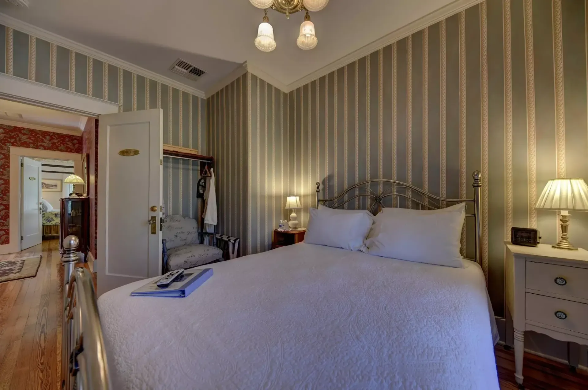 Bedroom with striped wallpaper, bed, nightstand, and doorway to another room.