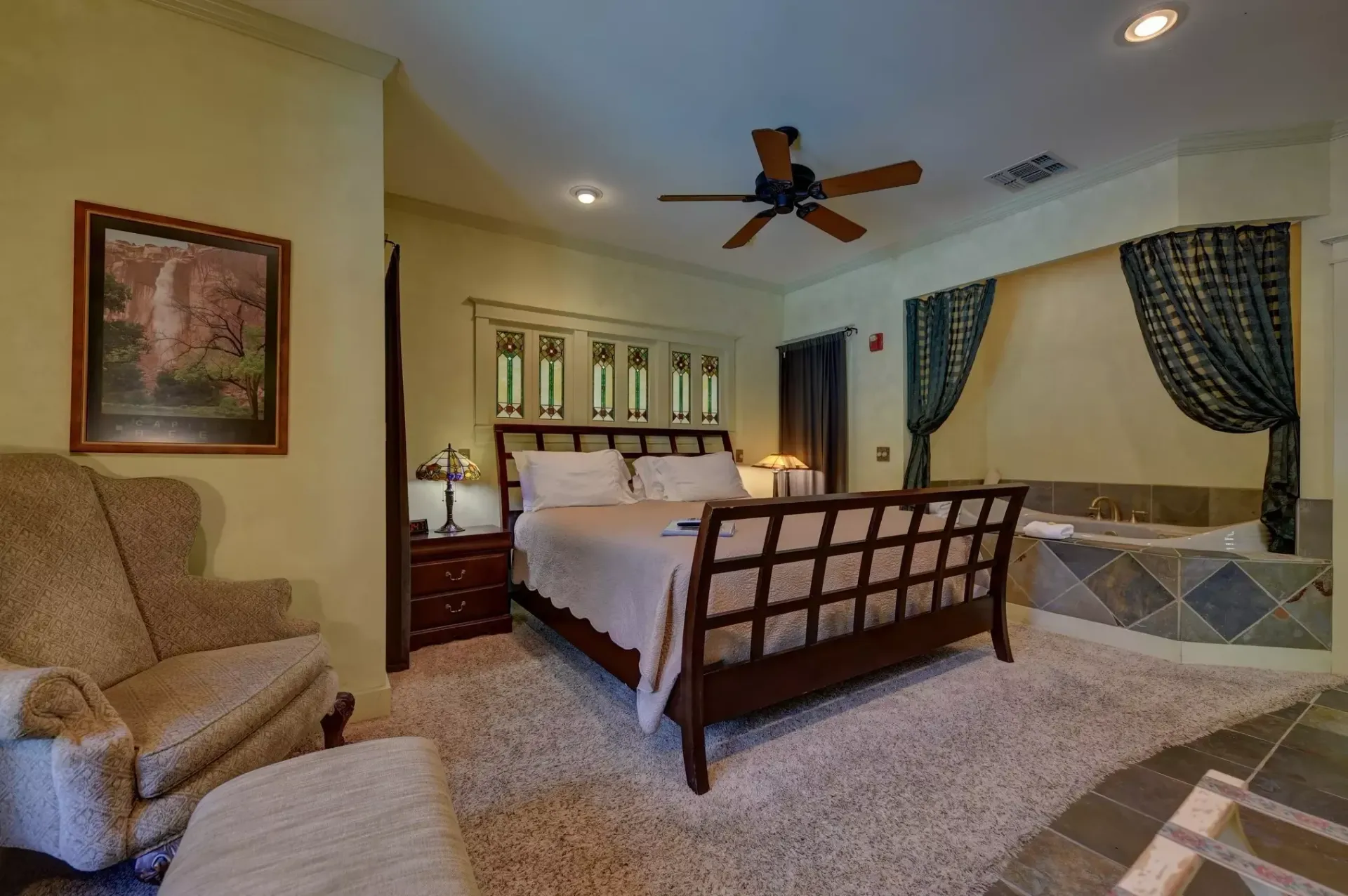 Bedroom with bed, armchair, and jacuzzi. Soft rug, neutral walls, dark wood bedframe.