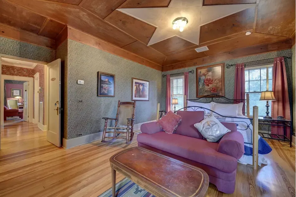 Bedroom with red sofa, bed, antique decor, star-shaped ceiling light, and doorway to another room.