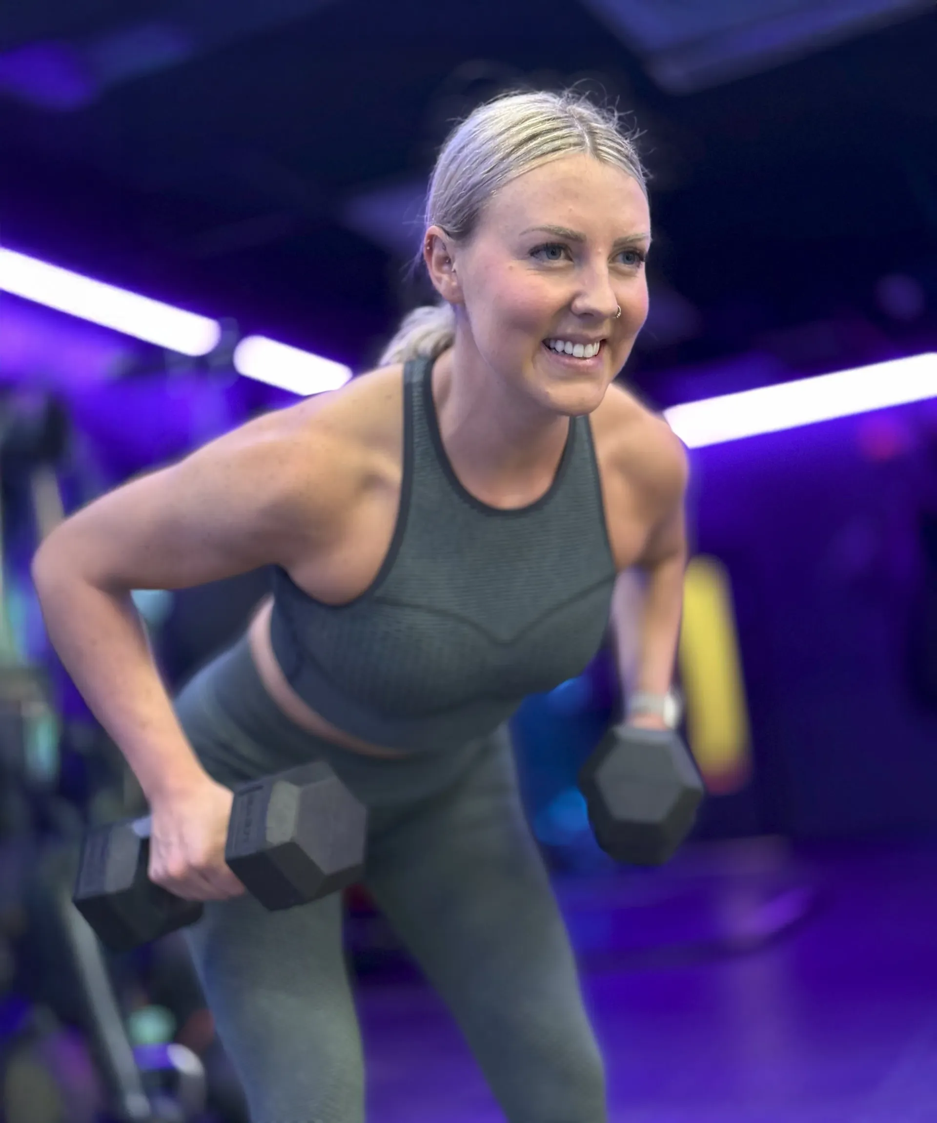 A woman is lifting dumbbells in a gym and smiling
