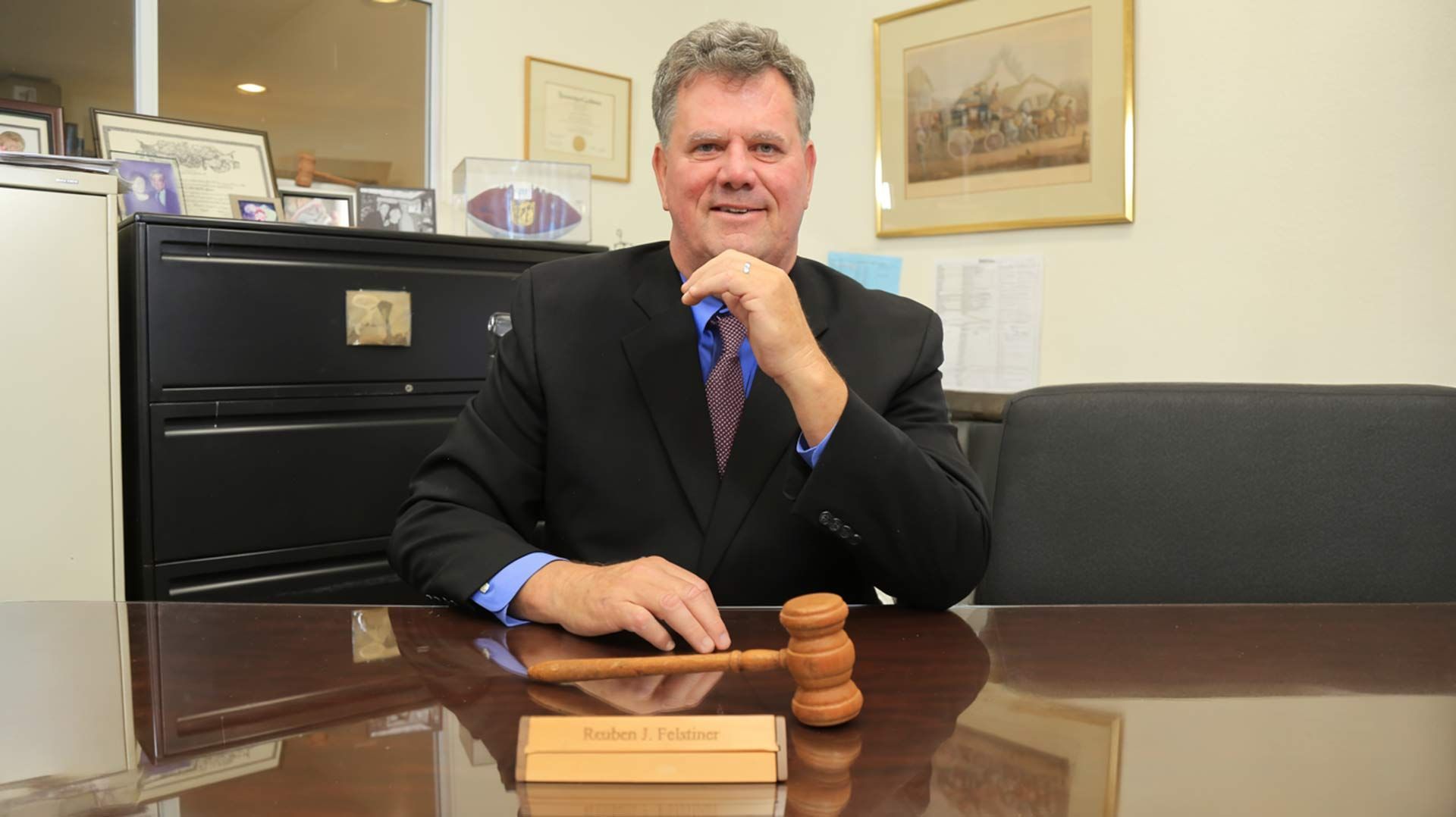 Man in suit at desk, holding gavel; office setting.