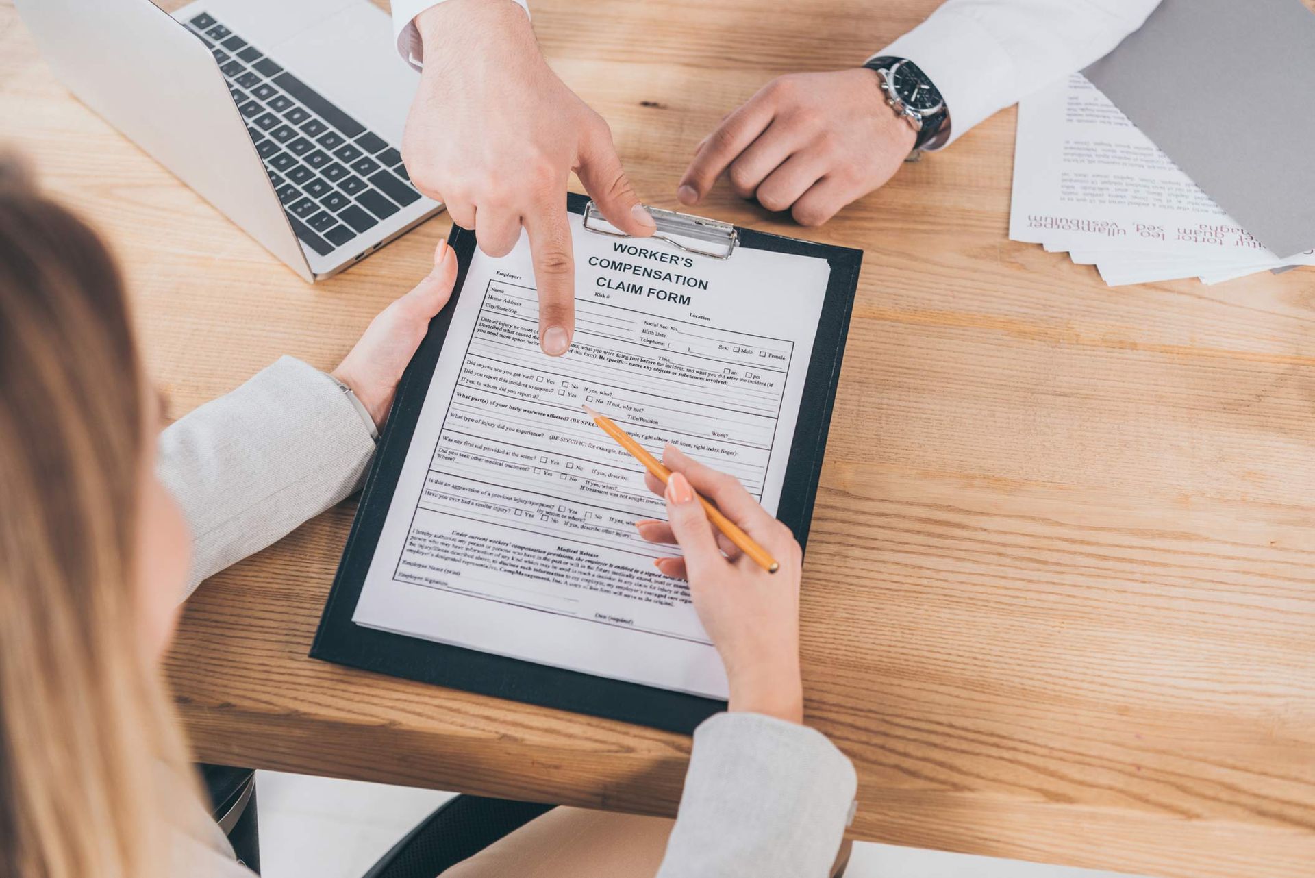 Two people reviewing paperwork at a wooden desk, one pointing, the other holding a pencil. Two people reviewing paperwork at a wooden desk, one pointing, the other holding a pencil.