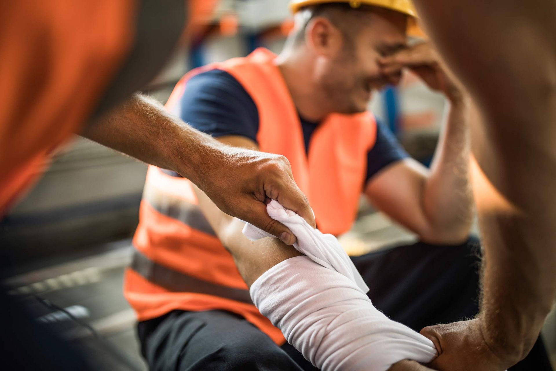 Worker with leg injury being bandaged by another worker at a construction site. Worker with leg injury being bandaged by another worker at a construction site.