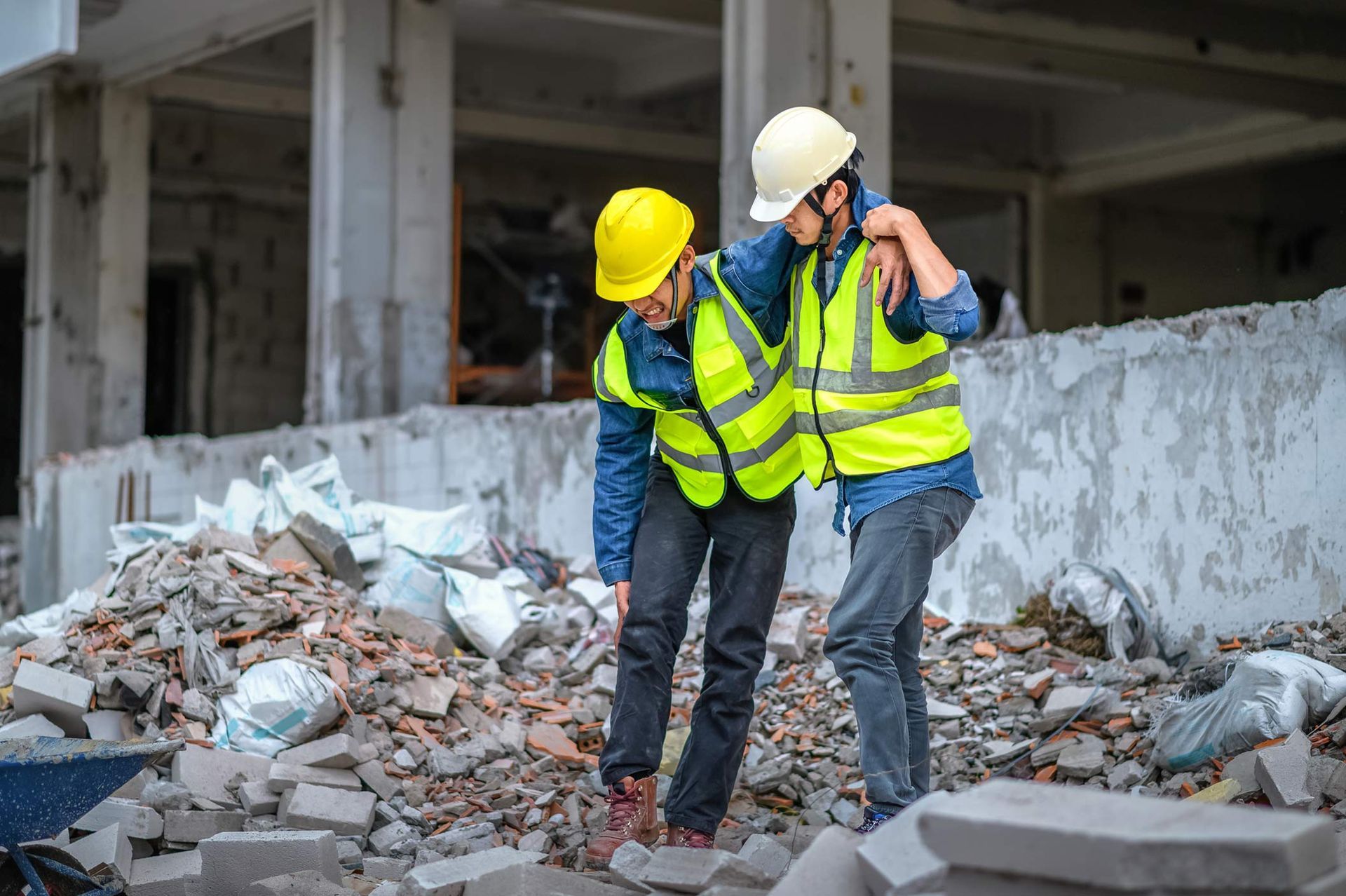 Construction worker helping an injured colleague. Both wear vests and helmets, rubble surrounds them in a building. Construction worker helping an injured colleague. Both wear vests and helmets, rubble surrounds them in a building.