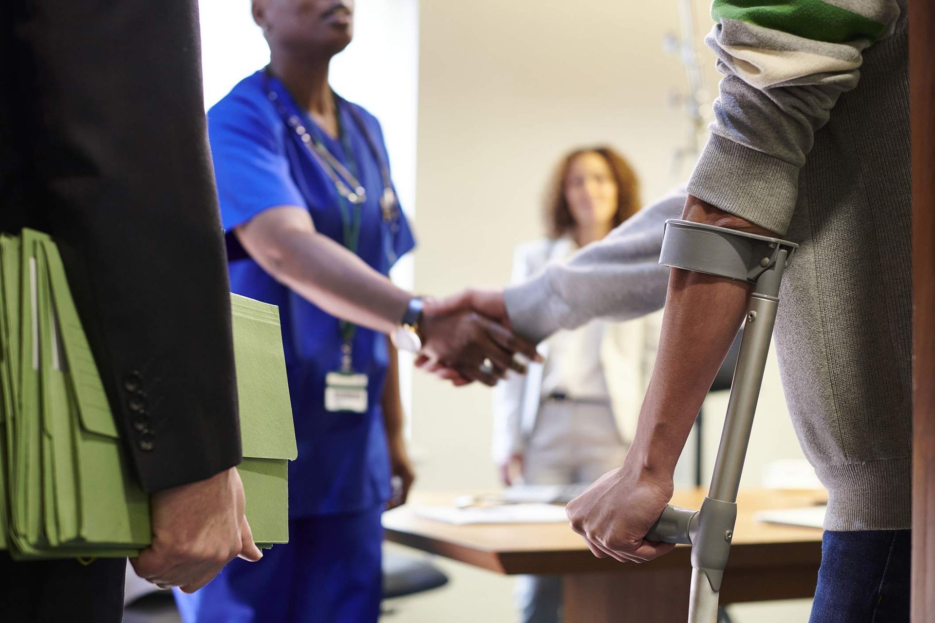Person on crutches shakes hands with someone in medical scrubs, others watch. Person on crutches shakes hands with someone in medical scrubs, others watch.