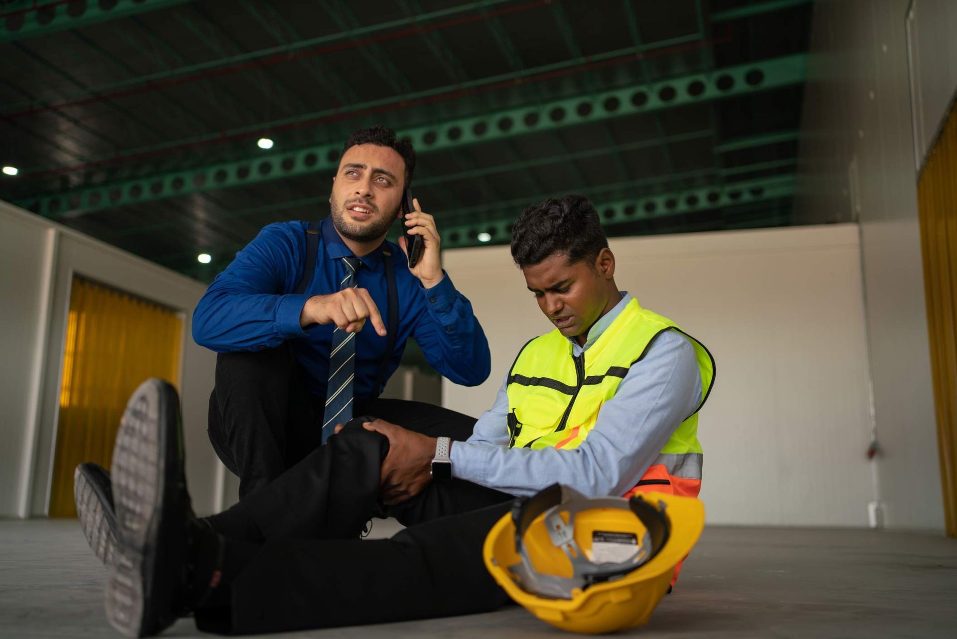 Man on phone calls for help for injured worker with knee injury. Construction site. Man on phone calls for help for injured worker with knee injury. Construction site.