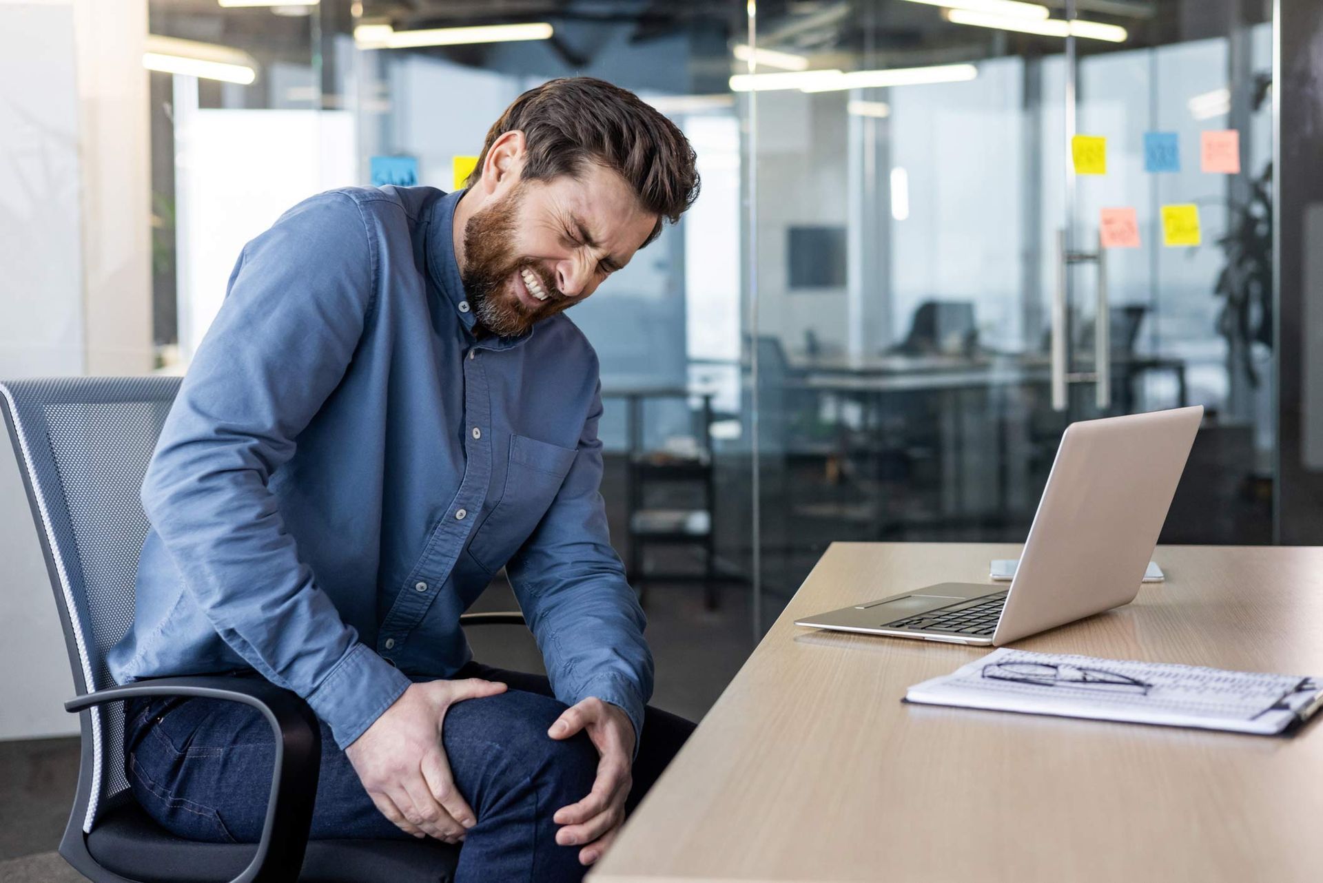 Man clutching knee in pain, seated at desk in office setting.
